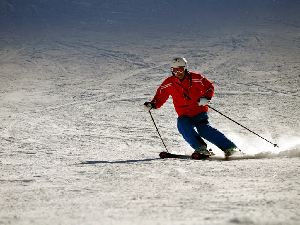 Skifahrer in roter Jacke zieht einen Schwung.